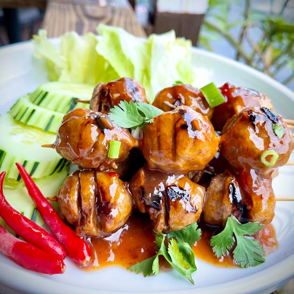 Thai meatballs on skewers with sweet chili sauce, cilantro, cucumber, and red chilies.